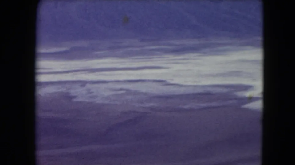 1961 8mm frame showing a bright horizontal cloud or surf band over distant water, with aged color and dark borders.