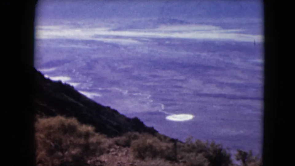 From Dante's View, the frame looks down across Badwater Basin with bright white salt flats visible in the distance.
