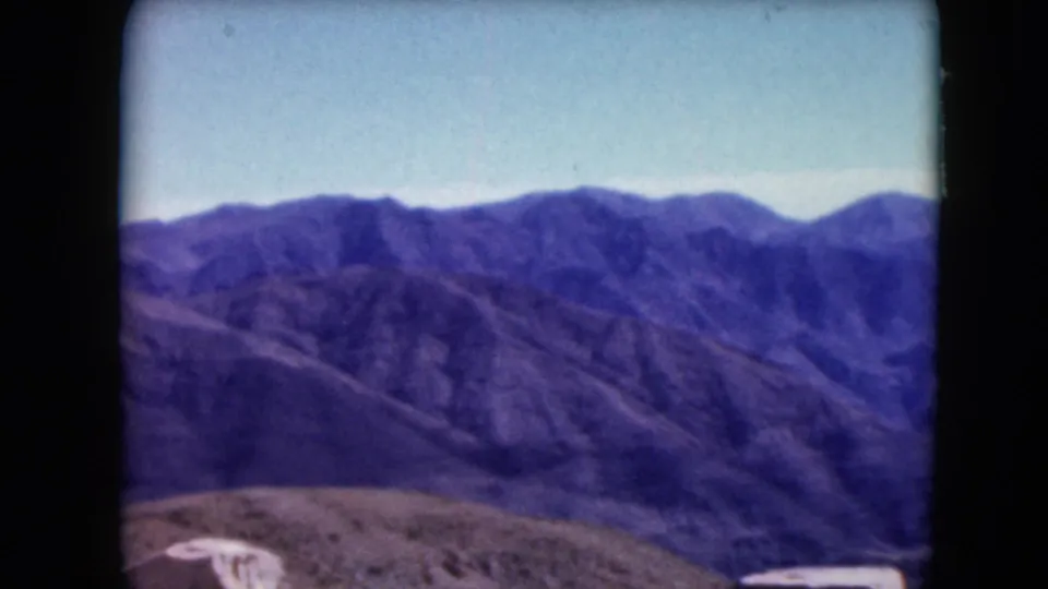 The camera looks across Nevada mountain ridges and a sunlit valley, with rocky foreground visible in the 1961 home movie frame.