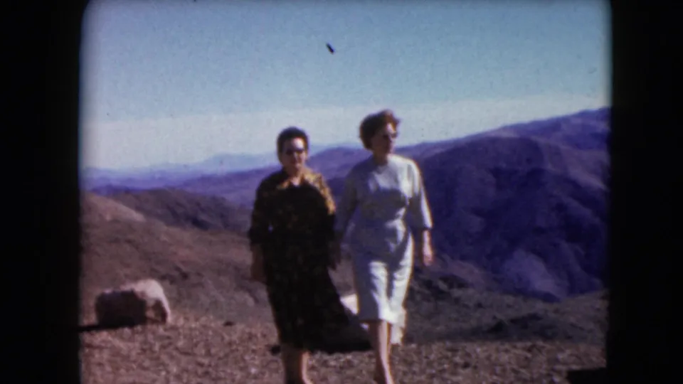 Two adult women in dresses stand on a Nevada hilltop in 1961, with rugged desert mountains stretching behind them.