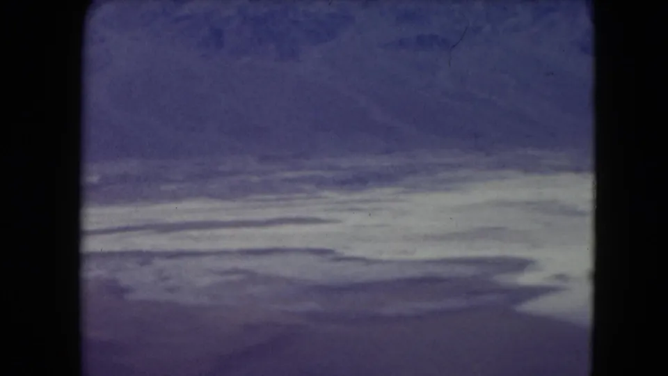 1961 Nevada 8mm frame showing a pale arid plain under a purple-blue sky, with soft grain and heavy gate edges.