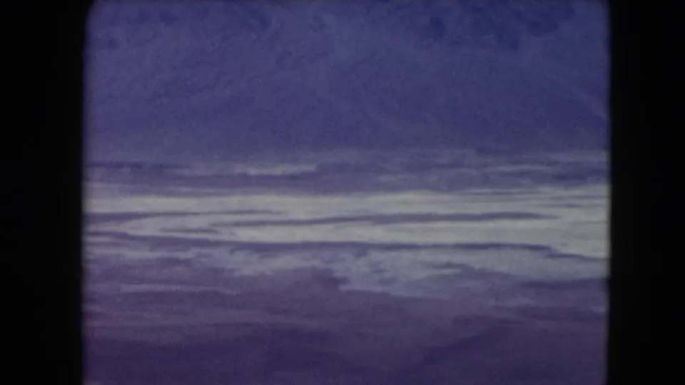 1961 Nevada landscape frame with a flat pale desert or salt-like surface and deep purple-blue sky, seen through 8mm film texture.