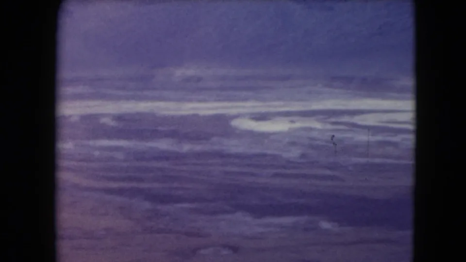 1961 Nevada frame showing dry open terrain with streaked pale surface texture, purple-blue sky, grain, and small film specks.