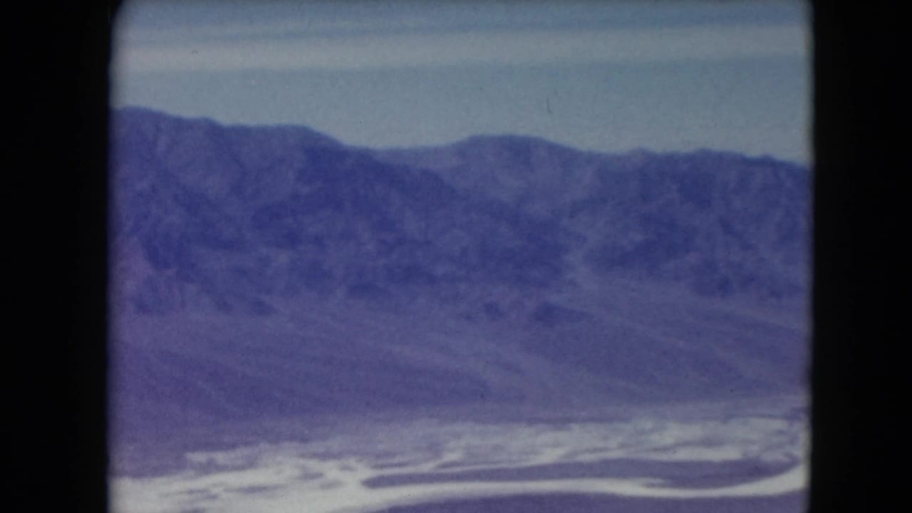 Distant purple mountain ridge above a pale valley and winding bright watercourse.
