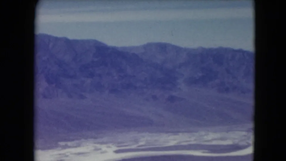 1961 Nevada 8mm frame showing distant desert mountains, pale sky, and a bright winding watercourse or flat below.