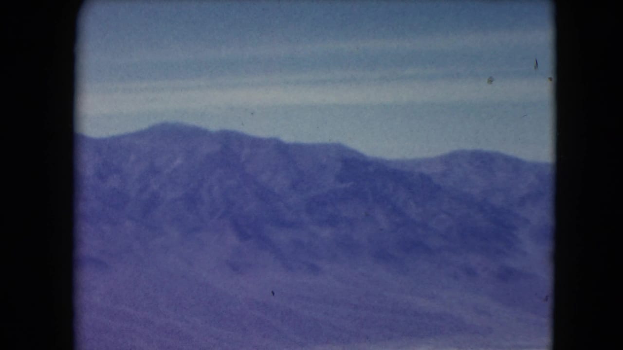 1961 Nevada 8mm view of a distant mountain range under pale sky, with aged color shift and film gate edges.