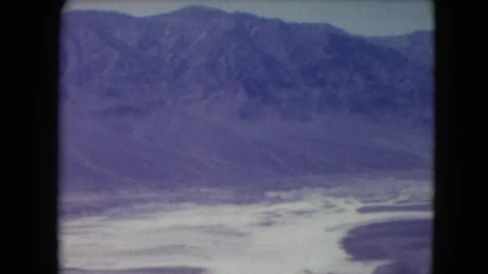 1961 Nevada 8mm frame with soft mountain ridges, pale basin floor, and a dark curved foreground landform.