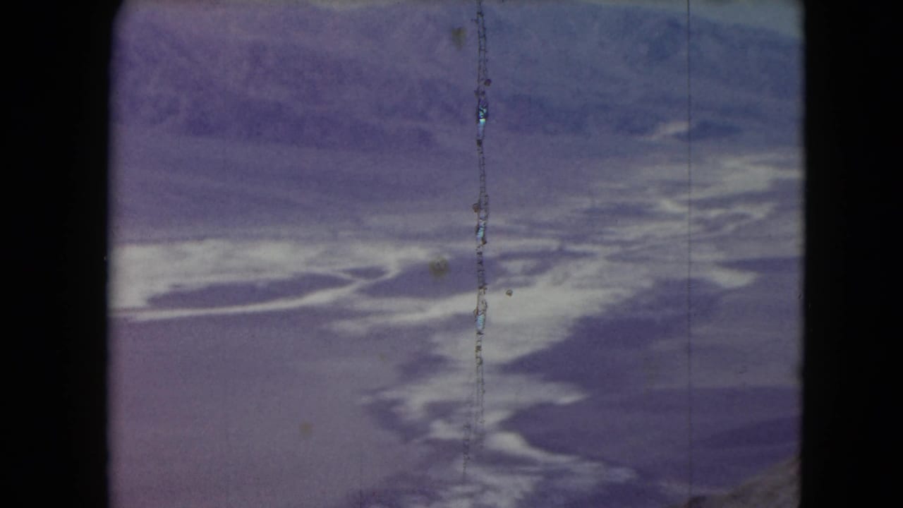1961 Nevada 8mm frame showing an aerial desert basin with white flats or water pools and distant mountains under a pale sky.