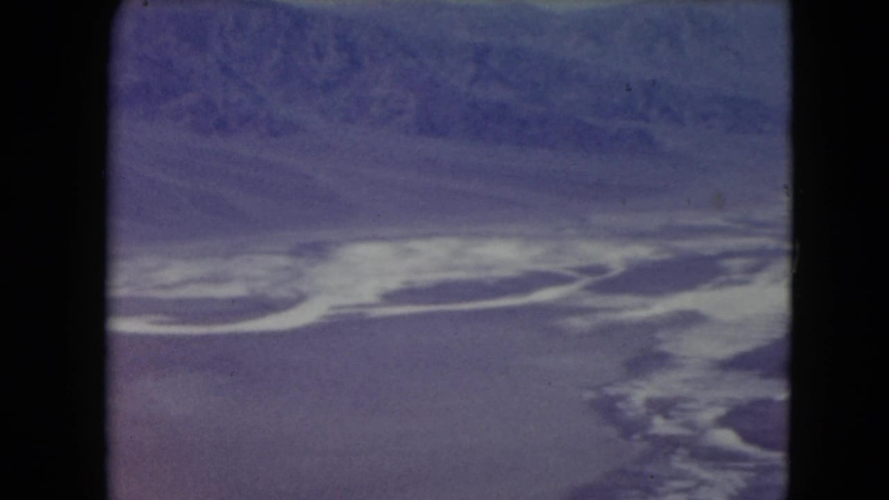 1961 Nevada aerial view with a winding white salt-flat or water feature set against purple desert terrain and a distant ridge.