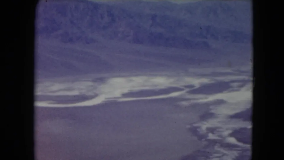 1961 Nevada aerial view with a winding white salt-flat or water feature set against purple desert terrain and a distant ridge.