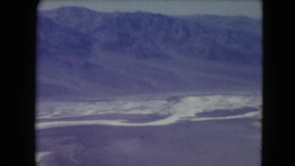 1961 Nevada 8mm frame showing a desert valley, hazy blue mountains, and a bright white pool or salt flat near the lower edge.