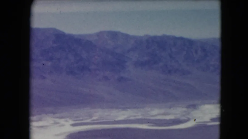 1961 Nevada aerial 8mm view of white flats or water pools in the foreground with hazy desert mountains beyond.
