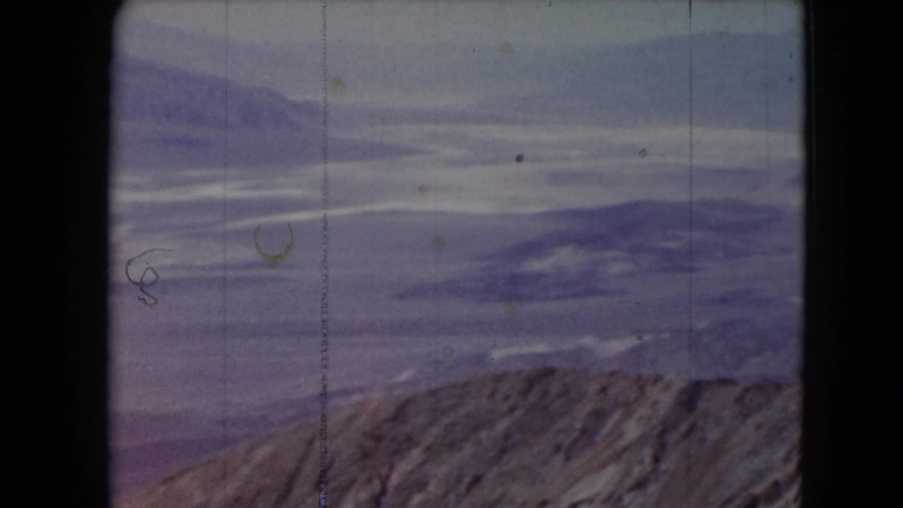 Distant blue-purple mountains beyond a rocky foreground under a pale sky.