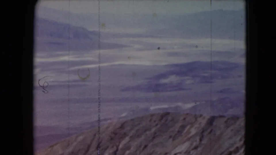 1961 Nevada 8mm frame showing layered mountain ranges, a rocky ridge, pale sky, and visible film scratches.