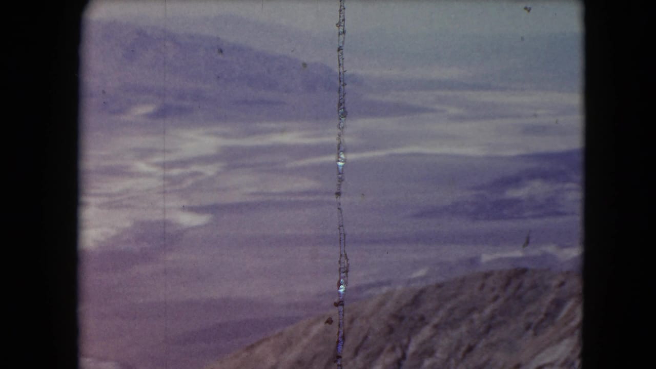Mountain ridge and distant hazy landscape with white cloud-like forms.