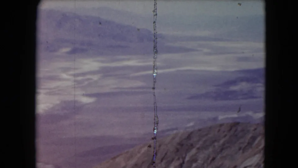 1961 Nevada 8mm frame with a rugged ridge, hazy distant mountains, pale sky, and vertical film wear.