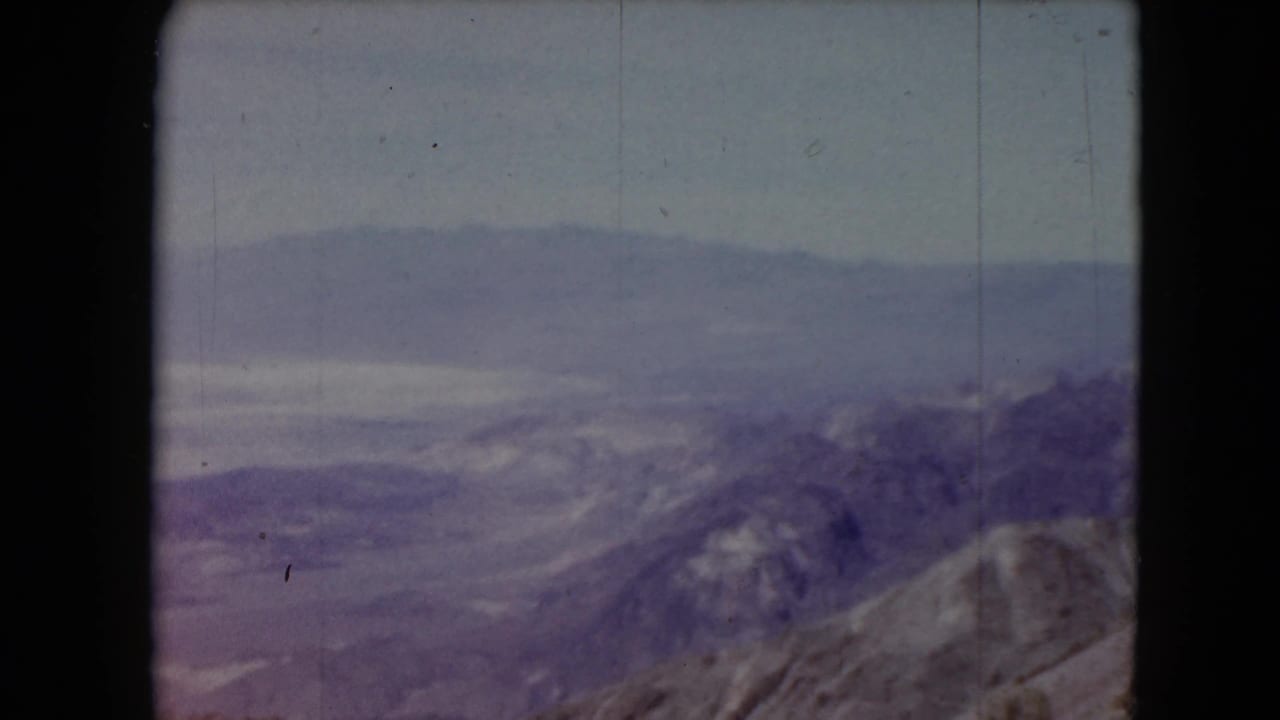 1961 Nevada 8mm frame showing distant mountain ridges and a muted hazy sky from a high vantage point.