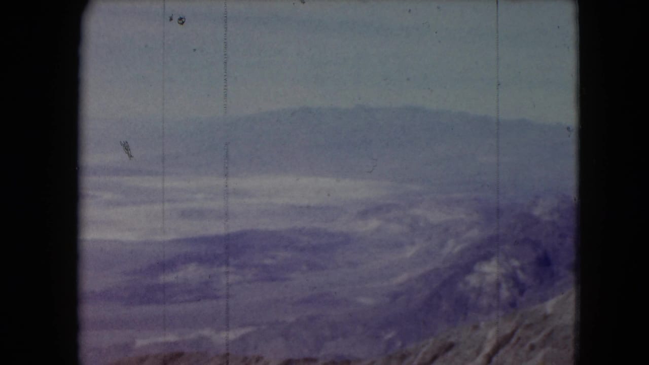 1961 Nevada landscape frame with layered ridges, pale sky, and visible 8mm film wear.