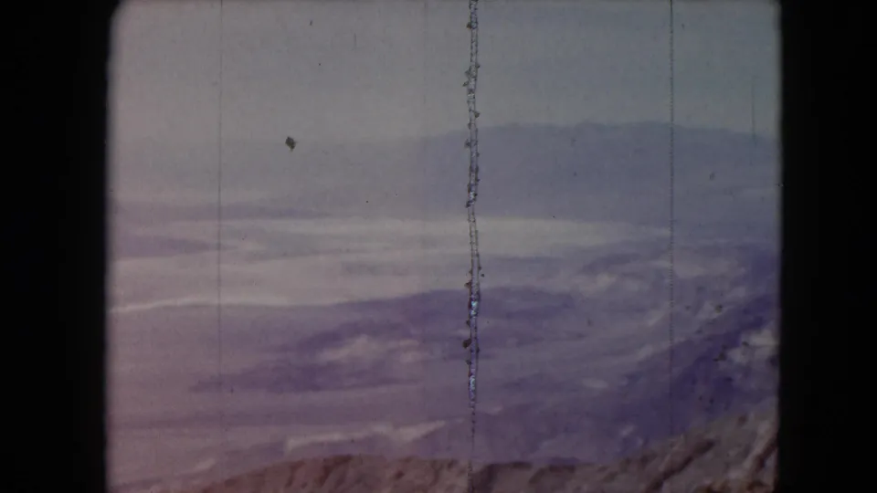 1961 Nevada 8mm view across pale ridges and desert mountains, marked by a prominent vertical film scratch.