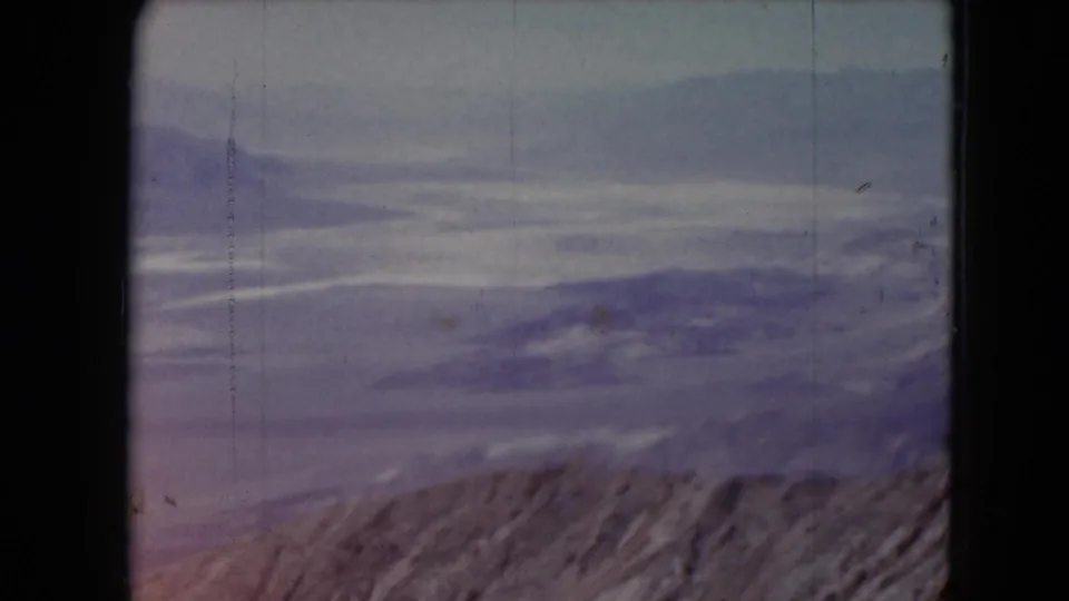 1961 Nevada 8mm frame showing a rocky ridge in front of softer distant mountain layers and hazy sky.