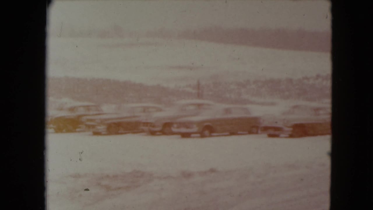 Faded 1961 Nevada home-movie frame of cars lined up in a snowy roadside parking area.
