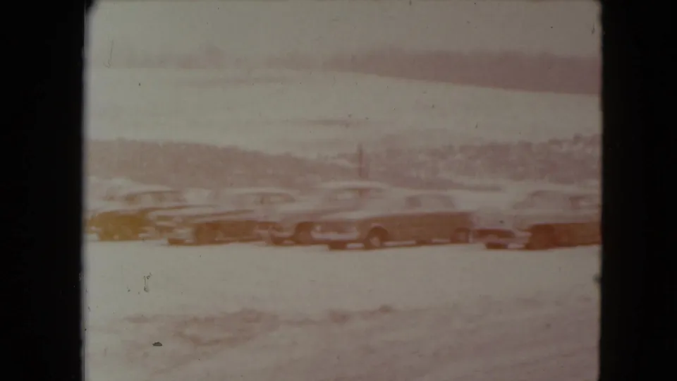 Faded 1961 Nevada home-movie frame of cars lined up in a snowy roadside parking area.