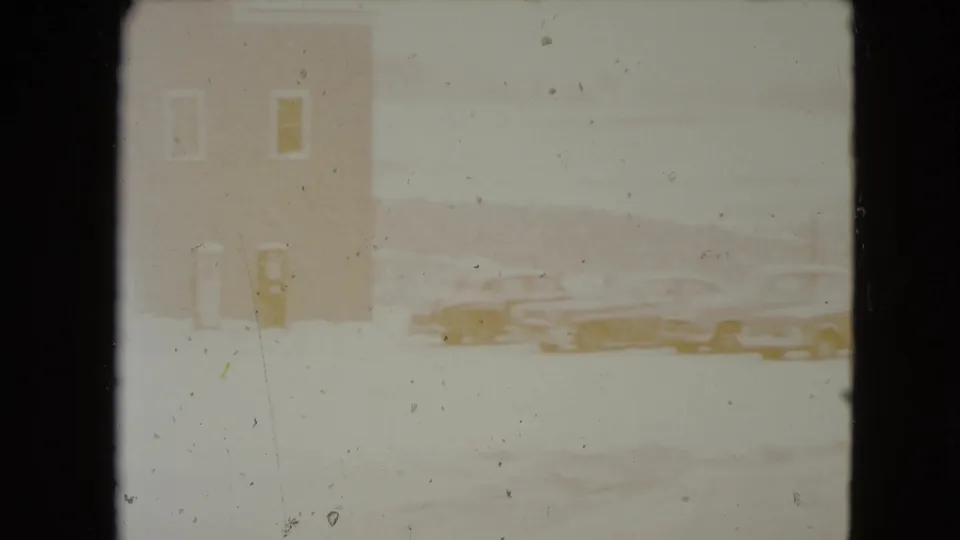 Overexposed 8mm frame of a plain building edge and classic cars parked in snow in Nevada.