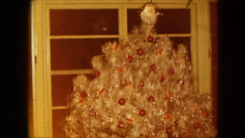 1961 Nevada home-movie frame focused on a silver tinsel Christmas tree with red ornaments and a small topper near a window.