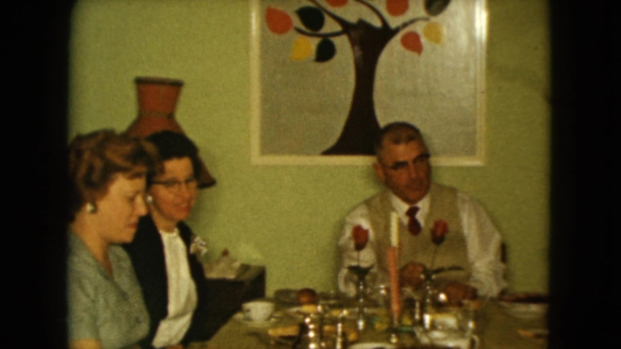 Two women and a man sit at a dining table beneath abstract tree artwork on a green wall.