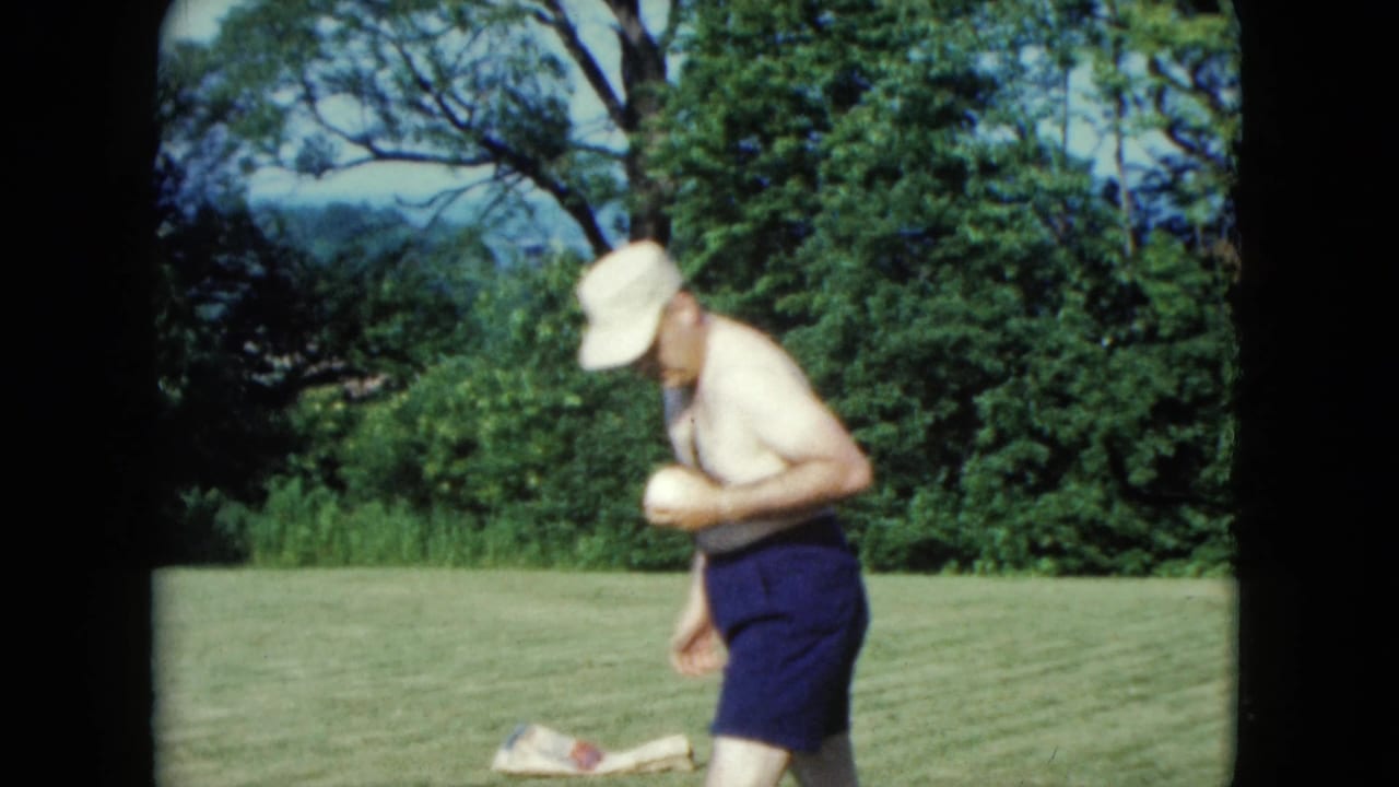 Man in white cap bends slightly while holding a ball on a grassy lawn.