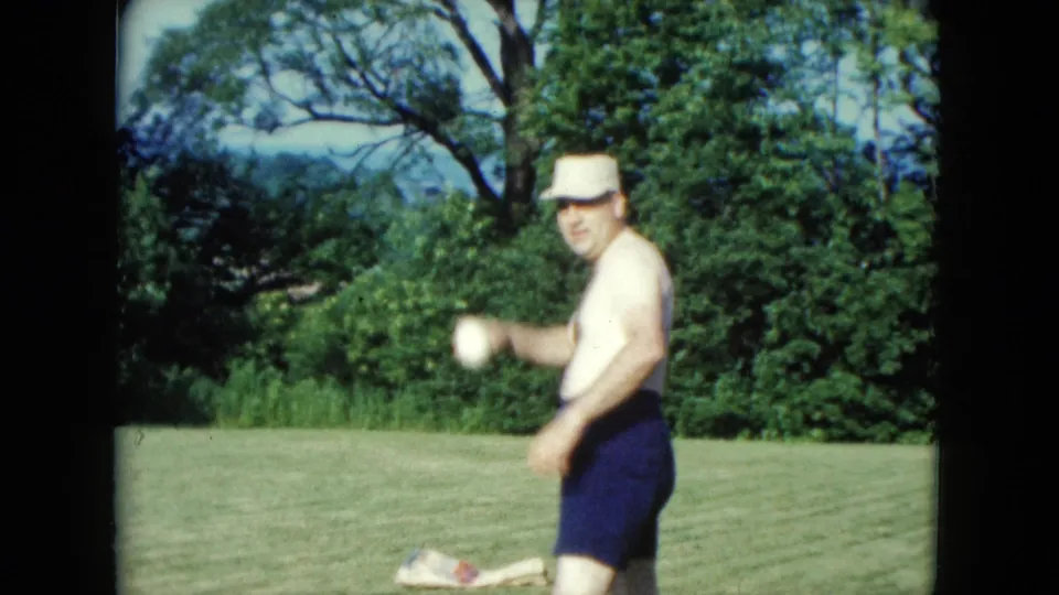 1961 Nevada frame showing the man turning toward the camera with a ball during a casual backyard game.