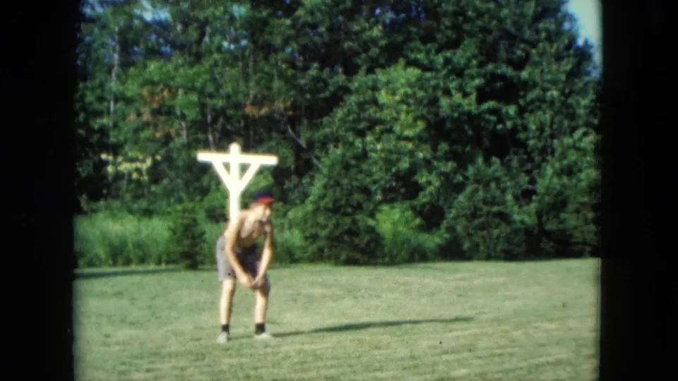 1961 Nevada home-movie frame showing a distant figure standing on the lawn during the catch game.