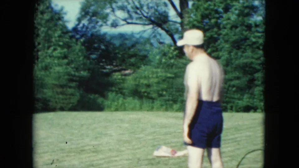 1961 Nevada home-movie frame showing a man in a white hat and dark swim trunks standing on a grassy lawn near trees.