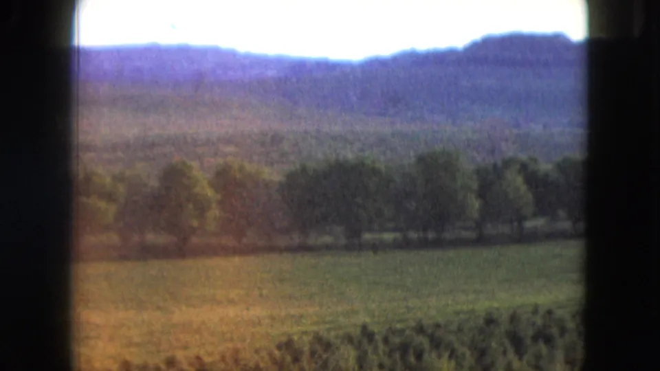 1961 Nevada 8mm frame with rolling fields, dark trees, blue hills, bright sky, and warm film coloration.