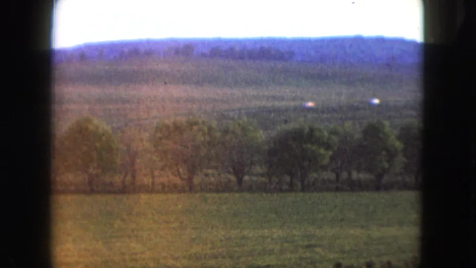 1961 Nevada rural view with pasture, trees, distant hills, and small white vehicles on a far road.