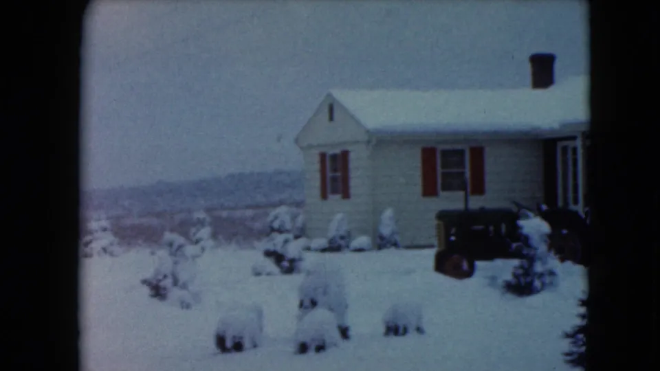 Jamestown, Wisconsin home-movie frame showing the side of a snow-covered house, a dark tractor, and a winter landscape beyond the yard.