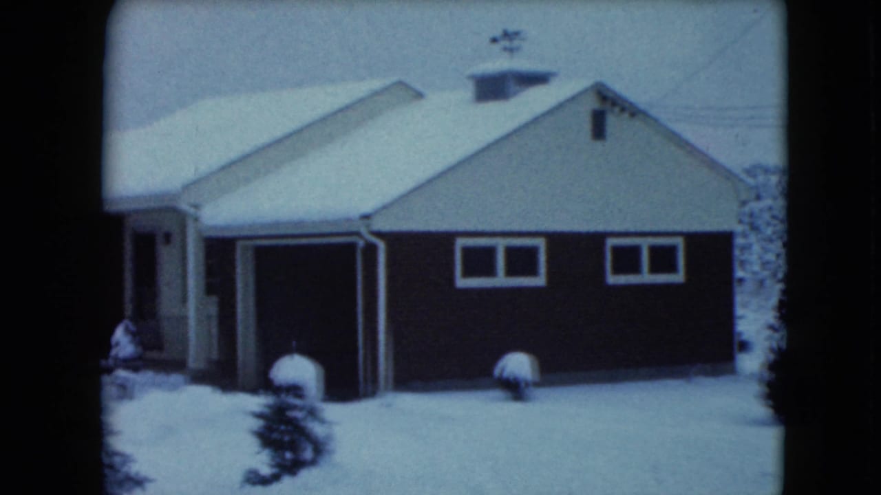1961 Jamestown, Wisconsin frame with the snow-covered garage, red side wall, small windows, and yard shrubs.