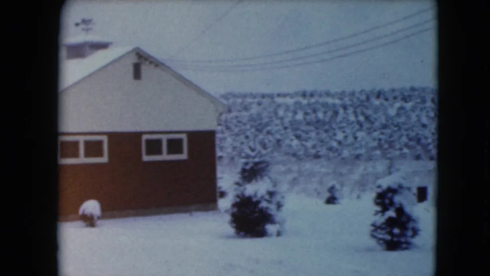 1961 Jamestown, Wisconsin frame showing a red-and-white rural building, snow-covered evergreens, utility lines, and distant wooded terrain.