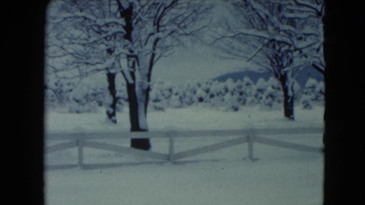 1961 Jamestown, Wisconsin 8mm frame showing a snowy rural yard, white rail fence, bare trees, and low hills beyond.