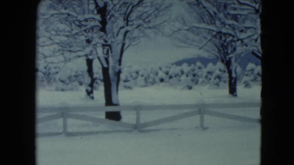 1961 Jamestown, Wisconsin 8mm frame showing a snowy rural yard, white rail fence, bare trees, and low hills beyond.