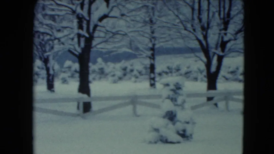 1961 Jamestown, Wisconsin 8mm frame showing deep snow, a white fence, leafless trees, and a small shrub in the foreground.