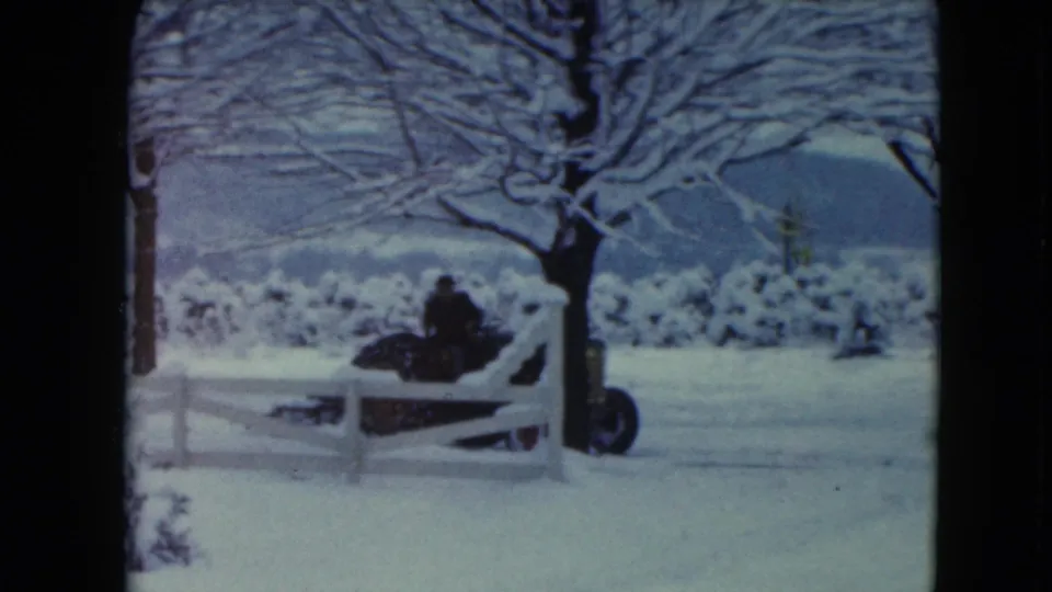 The tractor and seated driver pass near a white fence in the snowy Jamestown, Wisconsin rural landscape.