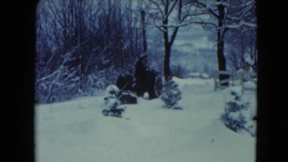 1961 Jamestown, Wisconsin 8mm frame showing a person driving a tractor through snow near bare trees and a white fence.