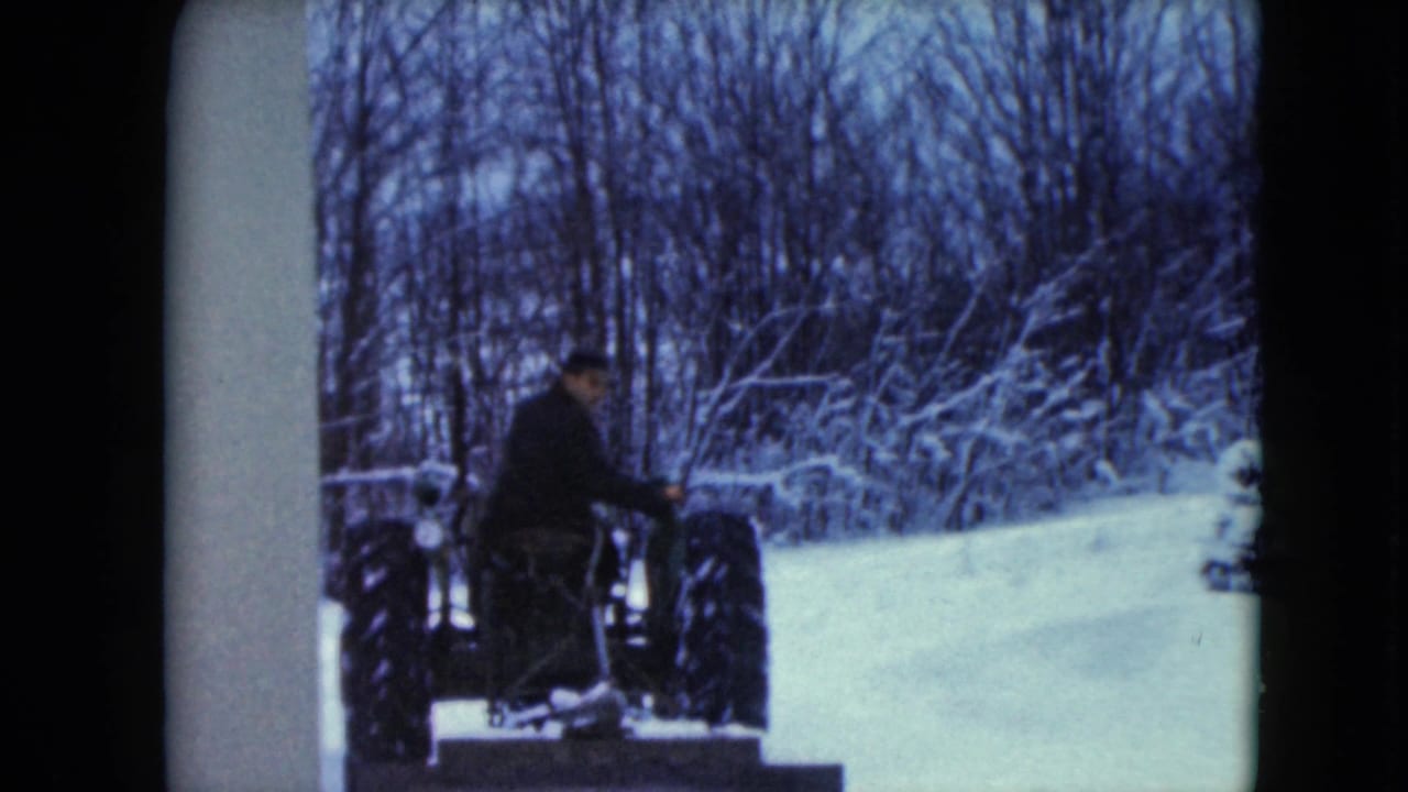 In 1961 Jamestown, Wisconsin, a man sits on a small tractor beside deep snow and bare winter trees.