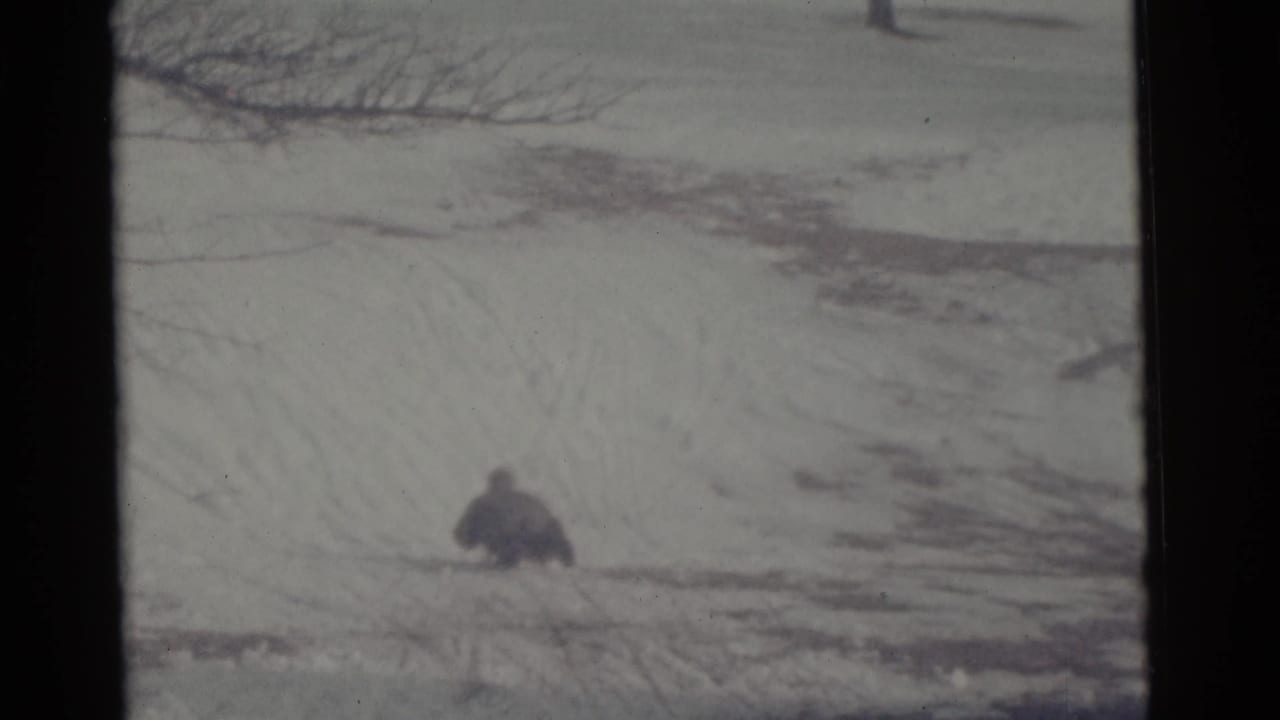 The sledder appears smaller in the 1961 Camden frame as they continue downhill across the snow under bare tree branches.