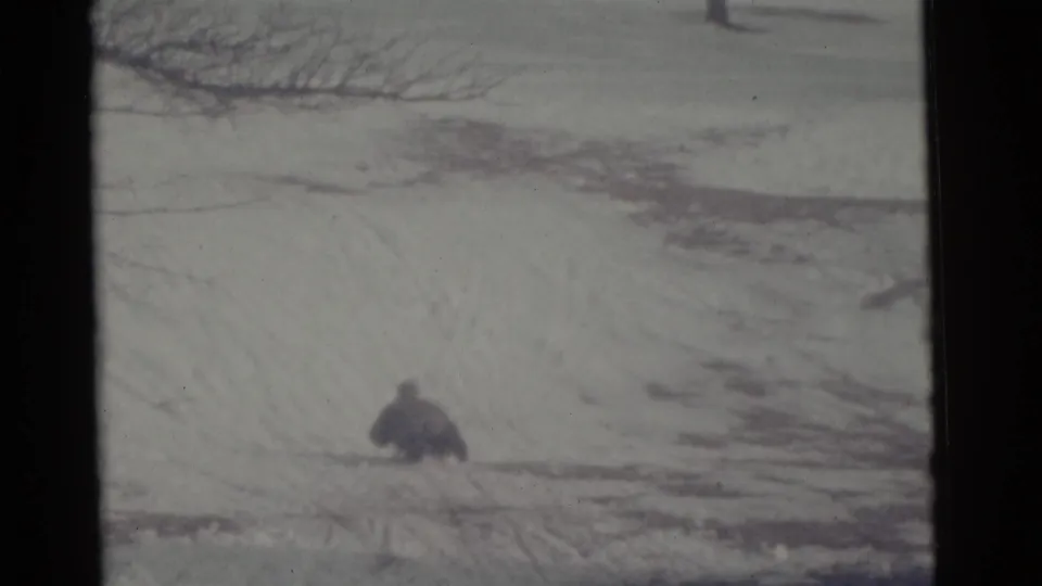 The sledder appears smaller in the 1961 Camden frame as they continue downhill across the snow under bare tree branches.
