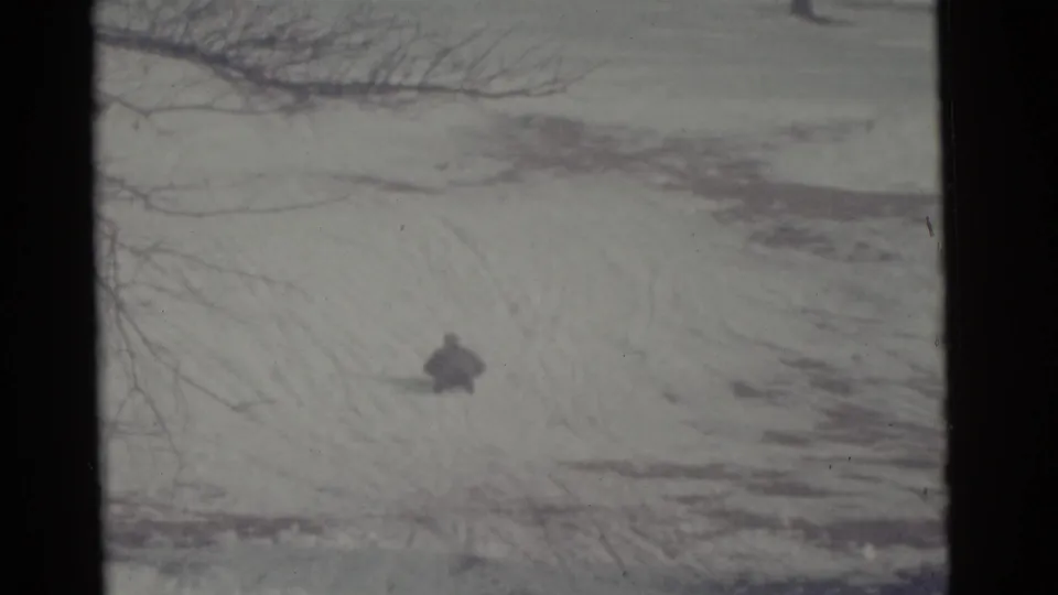 A distant sledder continues across the snowy Camden slope in this 1961 8mm frame, with bare branches crossing the upper edge.
