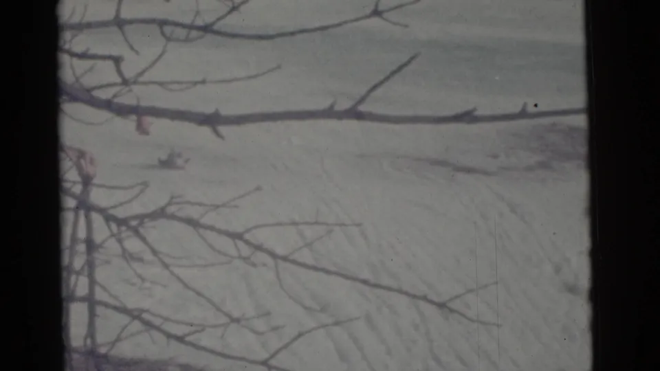 1961 Camden winter frame showing bare foreground limbs over a snow-covered hillside with subtle tracks.