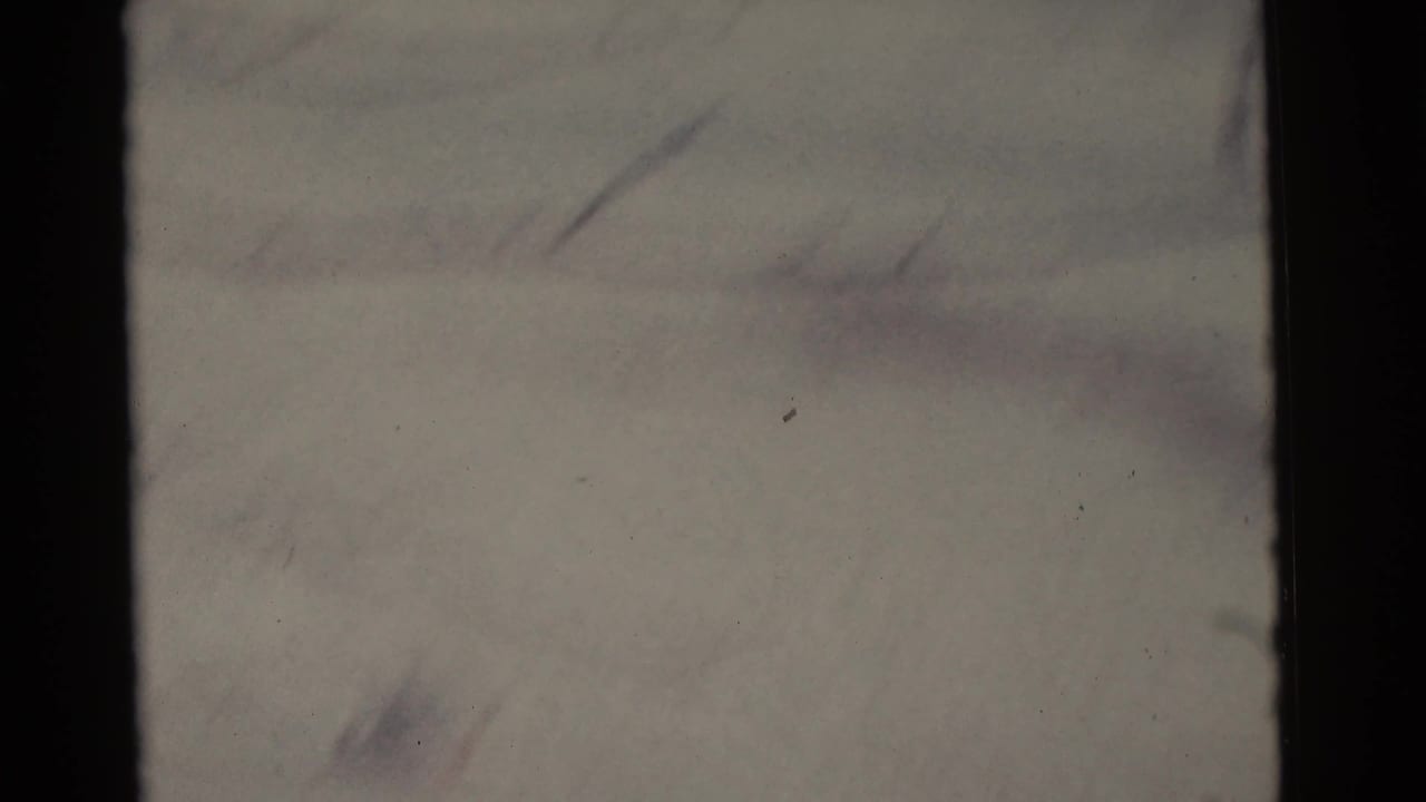 Soft snowy ground seen through dark film borders, with faint branches and tracks barely visible.