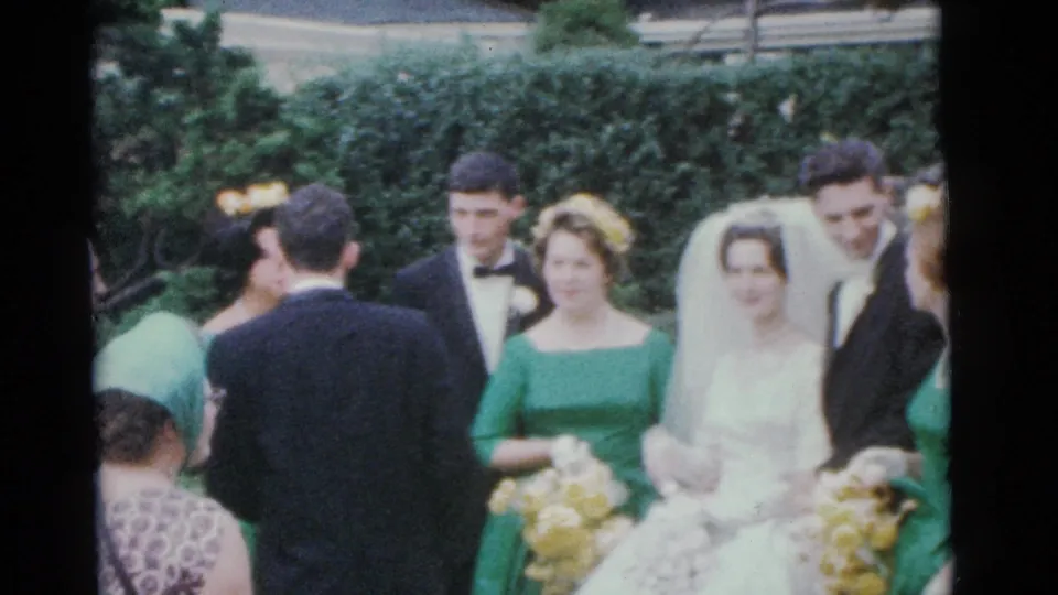 1961 Camden home-movie frame with the bride in a white gown and veil among tuxedoed attendants and green-dressed bridesmaids.